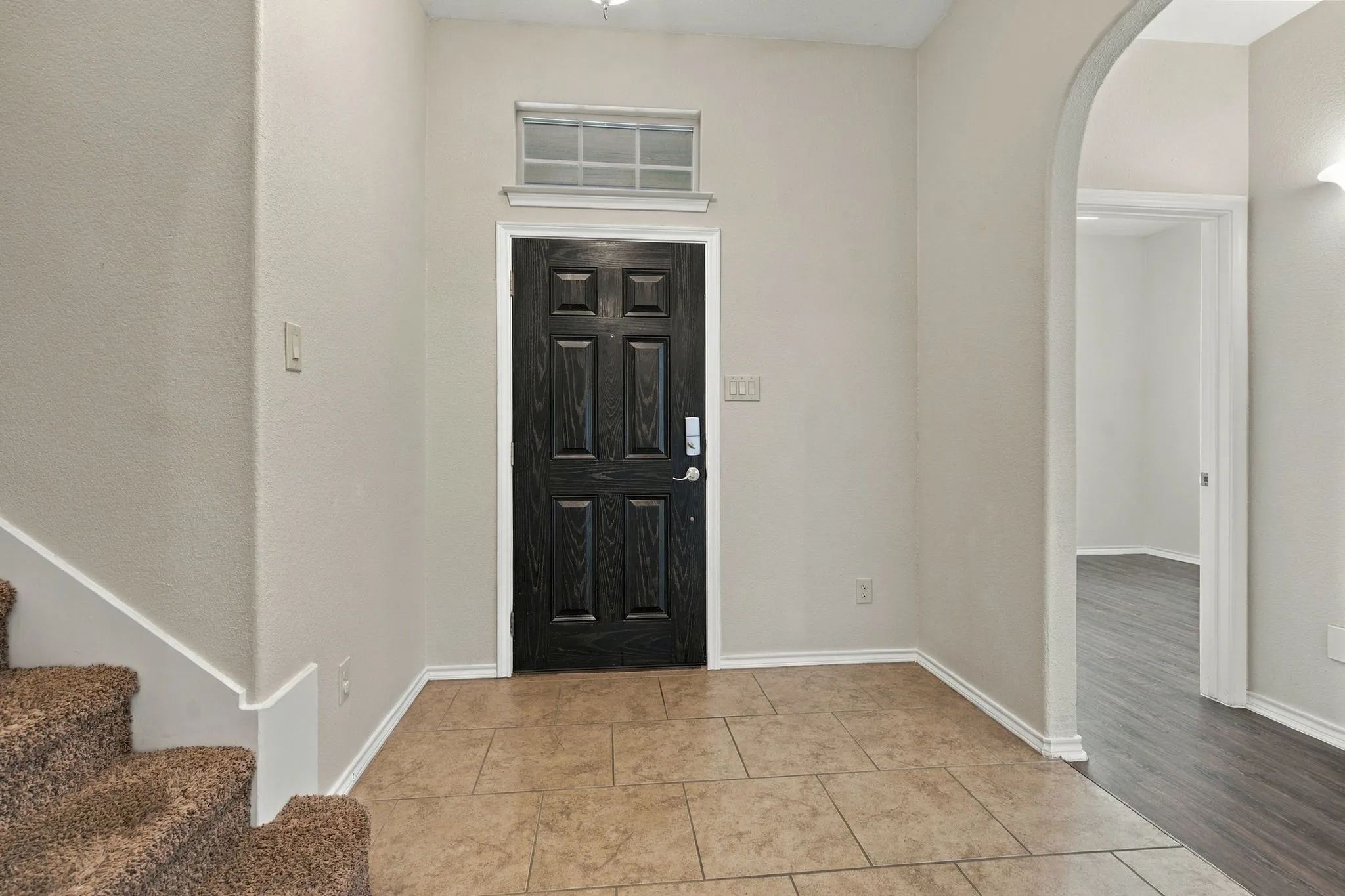 Tiled entryway with dark paneled door and transom window