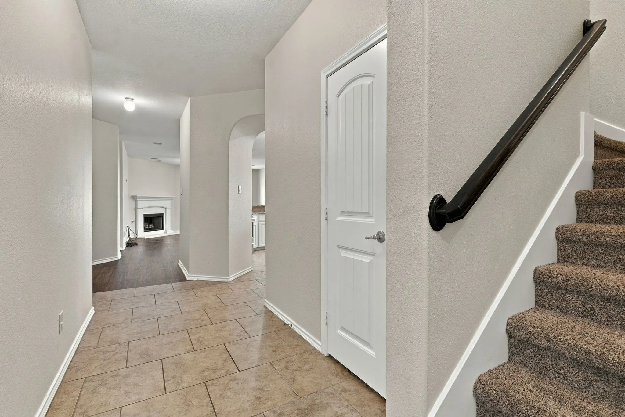 Neutral tone wall paint, tile flooring, interior door with paneling, carpeted staircase, and an archway