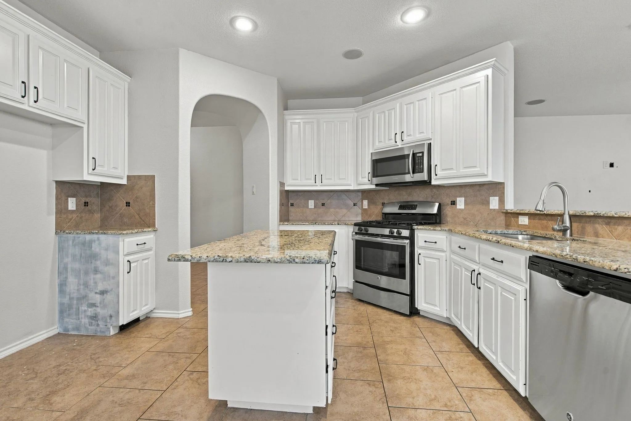 White cabinetry with black hardware, stainless steel appliances, a kitchen island with seating, recessed lighting, and tile flooring
