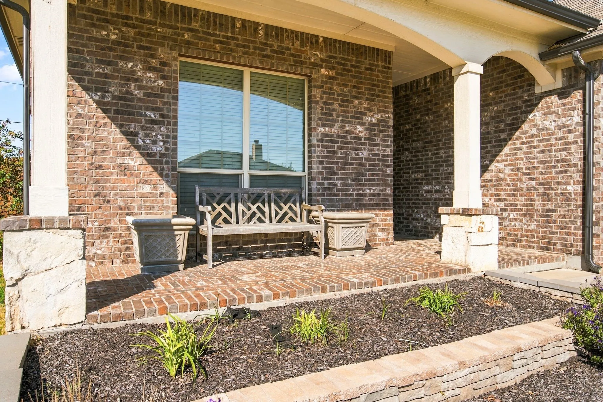 Brick exterior with a covered porch, brick pavers, stone-clad columns, and a landscaped planting bed