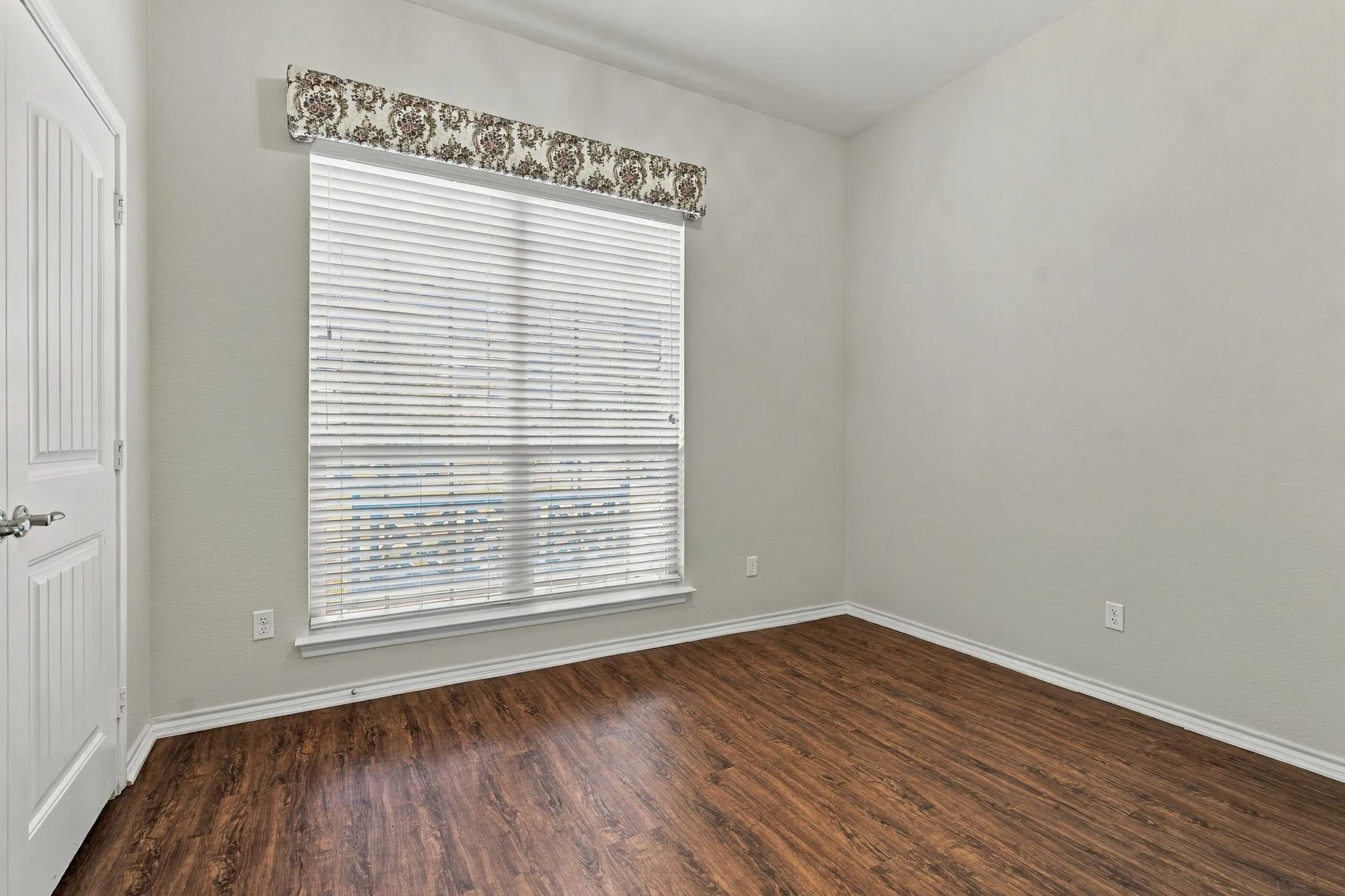Wood-finish flooring, white walls, and a window with blinds