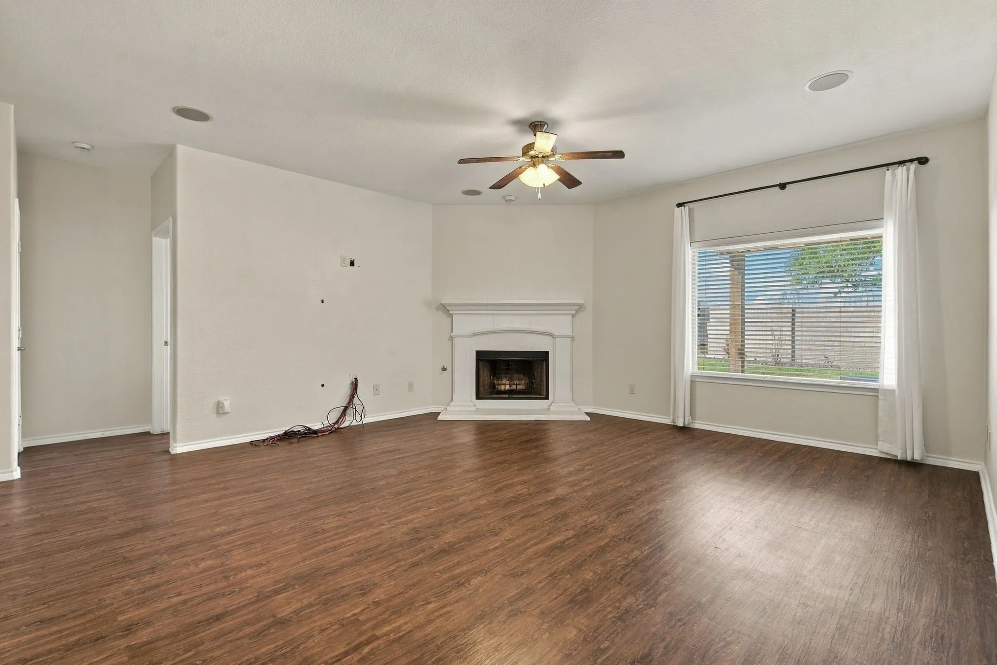 Wood-finish flooring, recessed lighting, and a corner fireplace with a white mantel