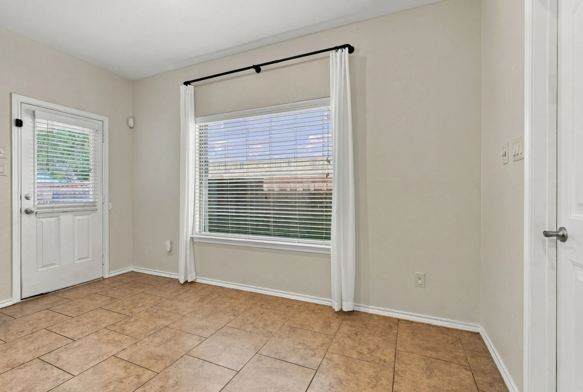 Tiled flooring, neutral wall tones, transom window over door, white door, and window with horizontal blinds