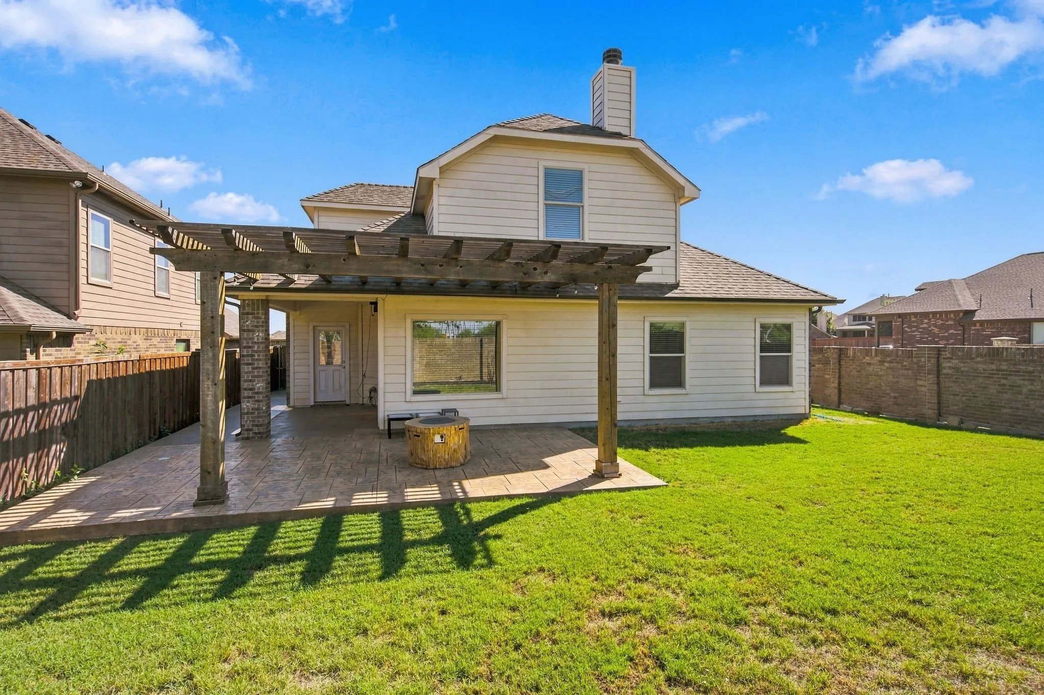 Expansive green lawn, stamped concrete patio, wood pergola, and a stone-clad column
