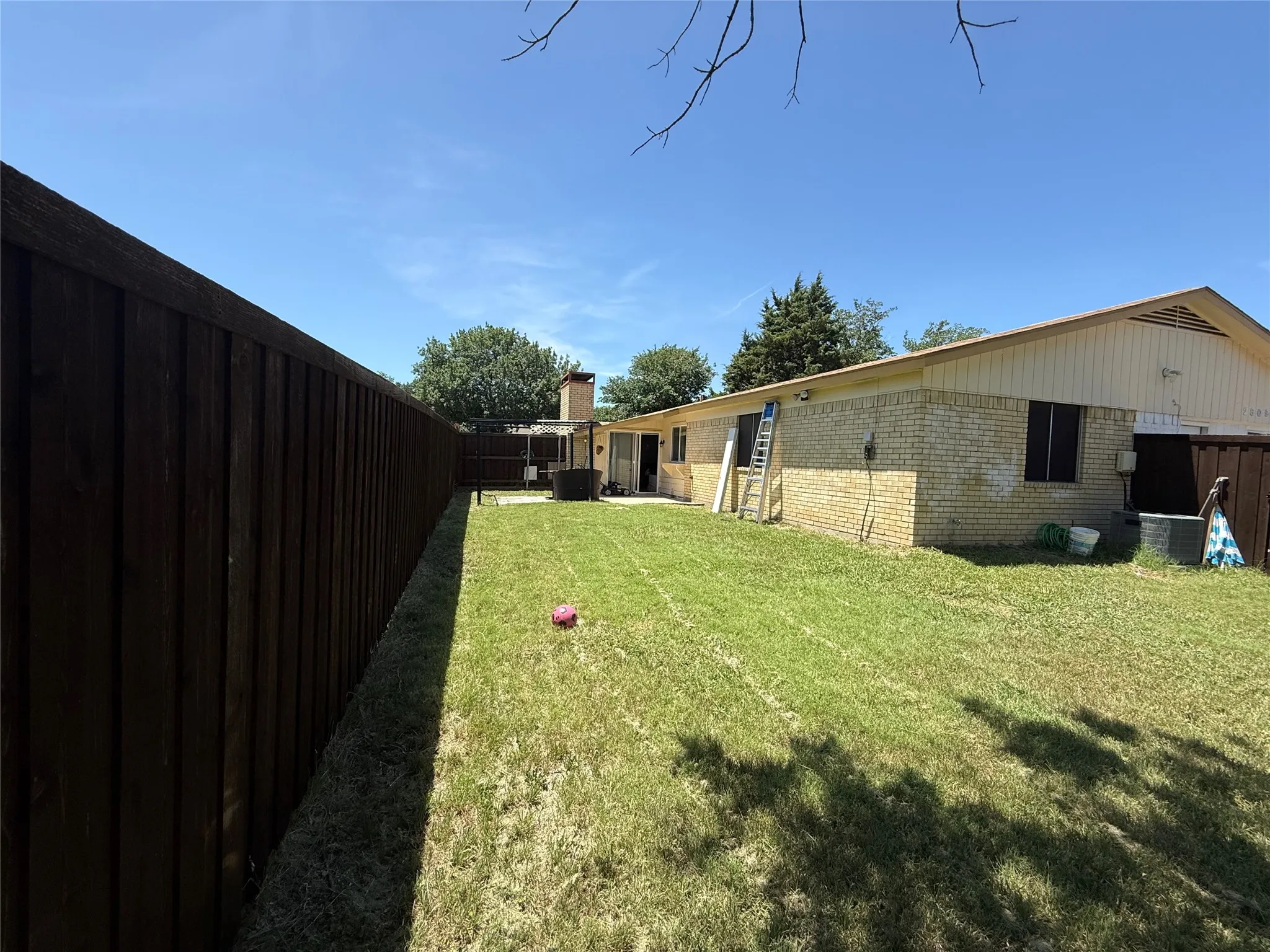 Expansive backyard with a manicured lawn, full-height privacy fencing, and a brick exterior