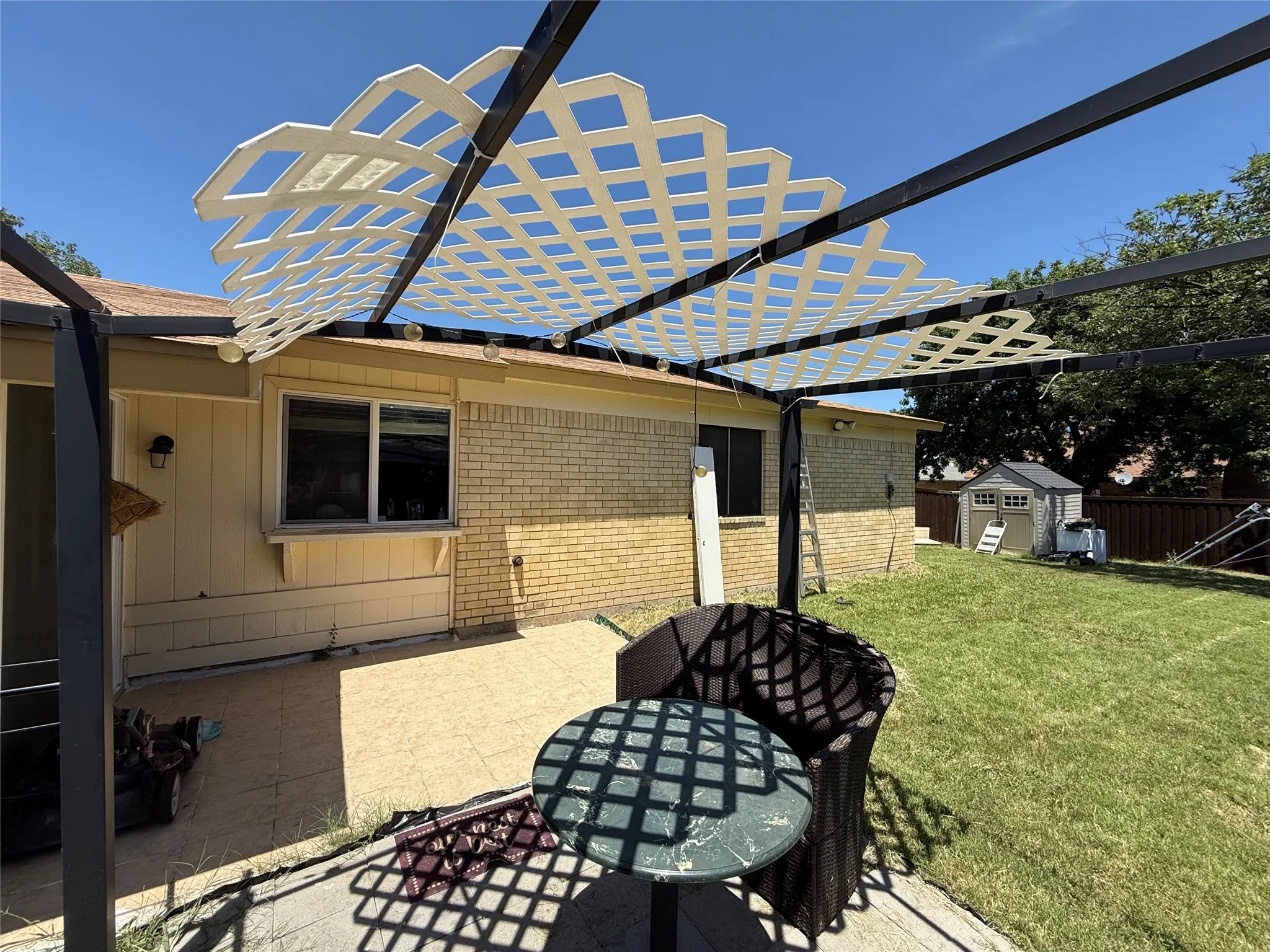 Outdoor patio with a lattice pergola, brick and siding exterior, and a grassy yard