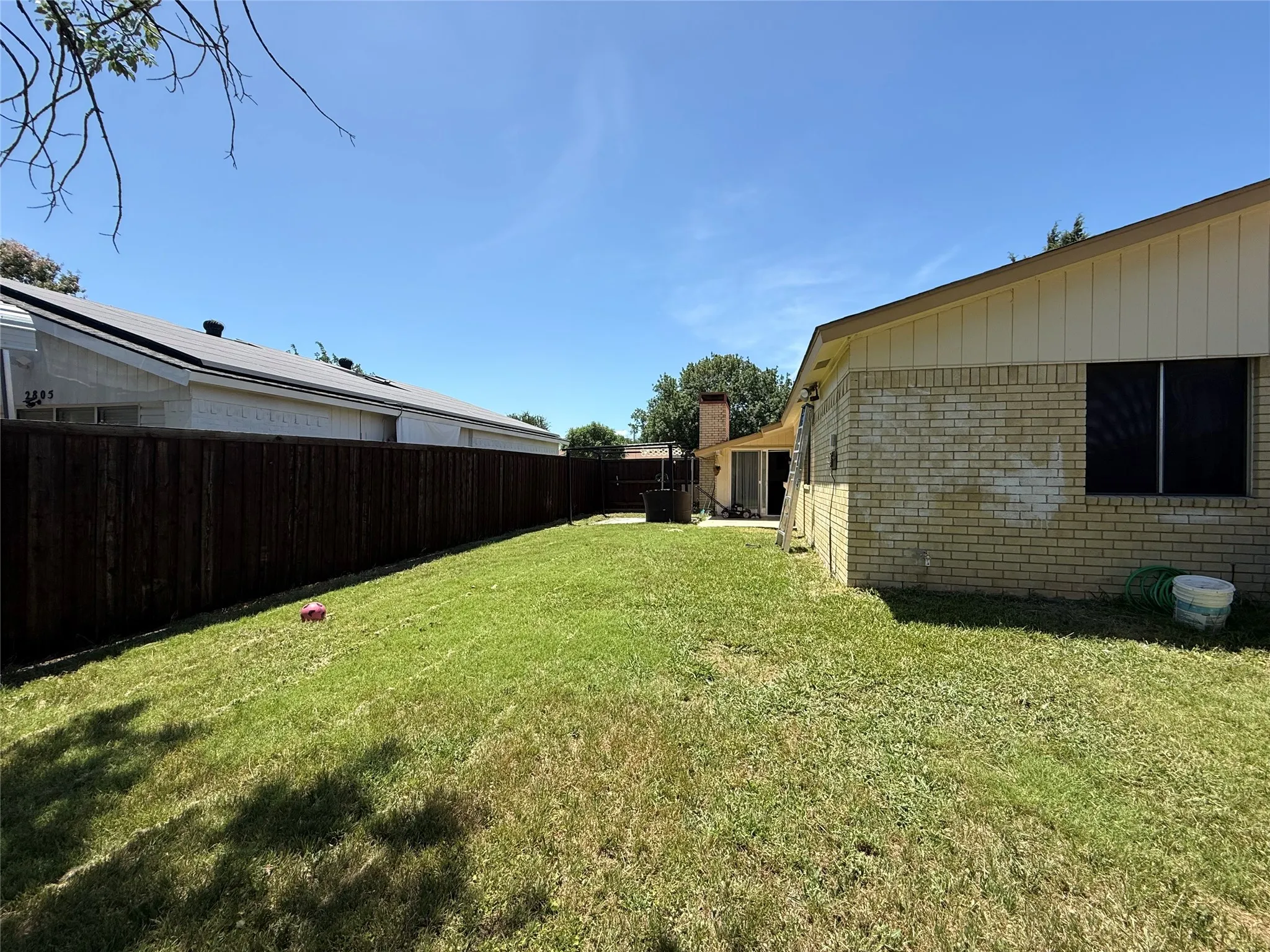 Spacious backyard with a wood privacy fence, featuring a manicured lawn and brick exterior