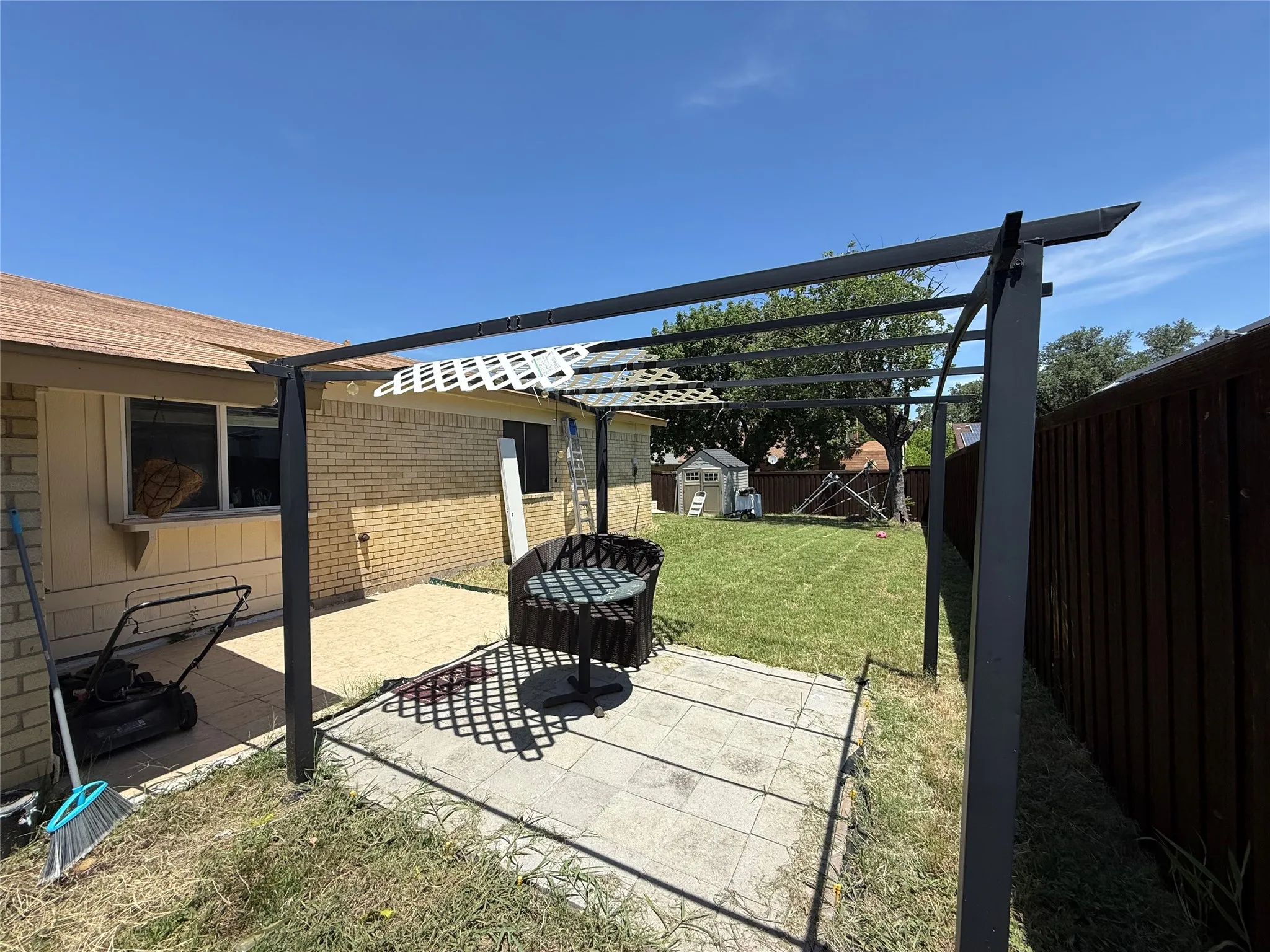 Paved patio area, metal pergola structure, brick exterior, and a wood privacy fence