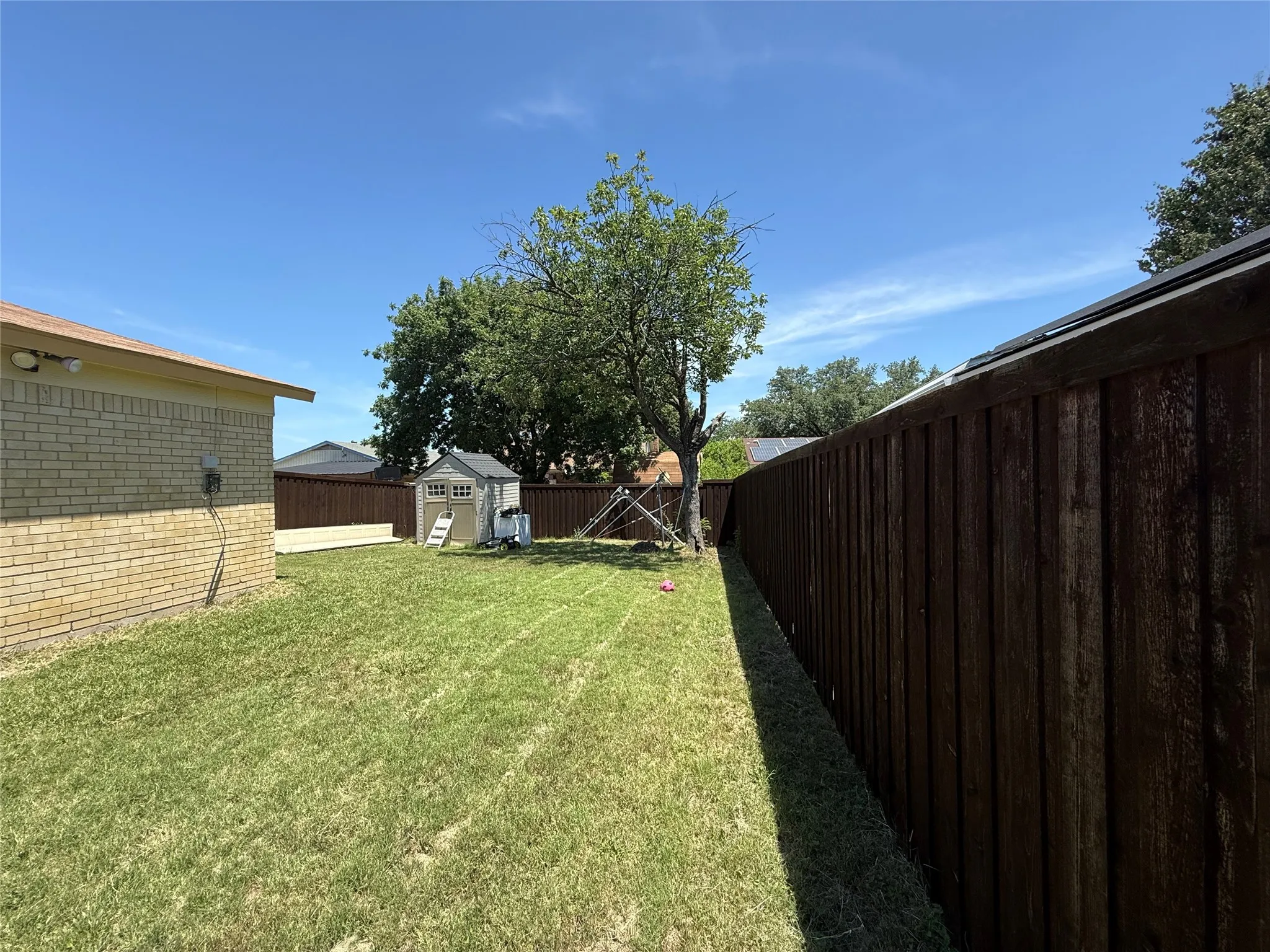 Expansive yard featuring a wooden privacy fence, mature trees, and a storage shed