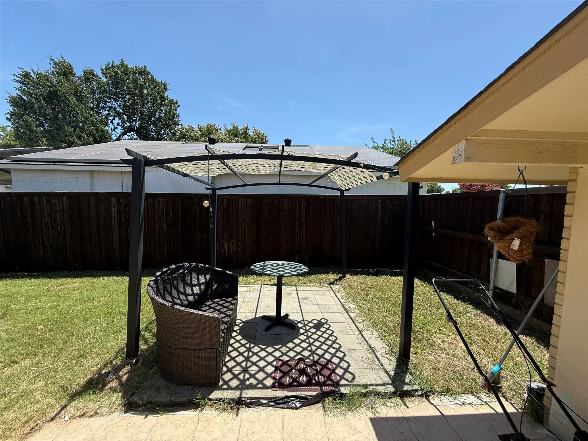 Backyard featuring a paved patio area, green lawn, wood fence, and a structured canopy