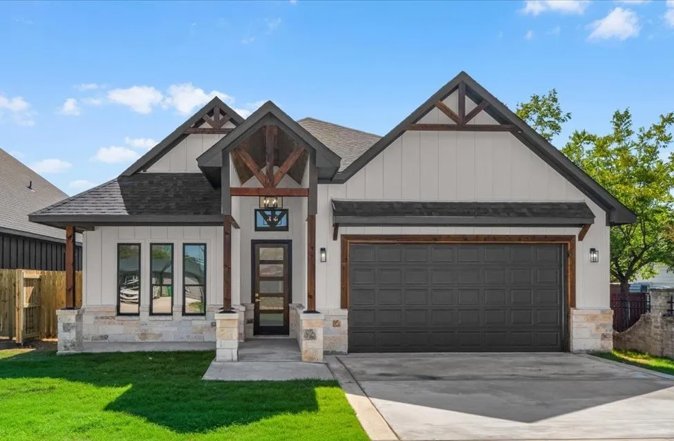 Modern farmhouse exterior with board and batten siding, stone facade accents, dark asphalt shingle roof, and a two-car garage