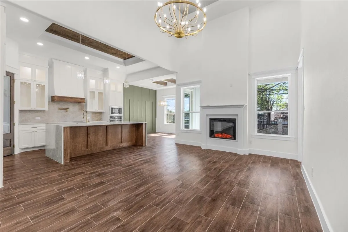 Spacious interior featuring wood-finish tile flooring, a kitchen island with stone countertops, white cabinetry, a built-in fireplace, and high ceilings
