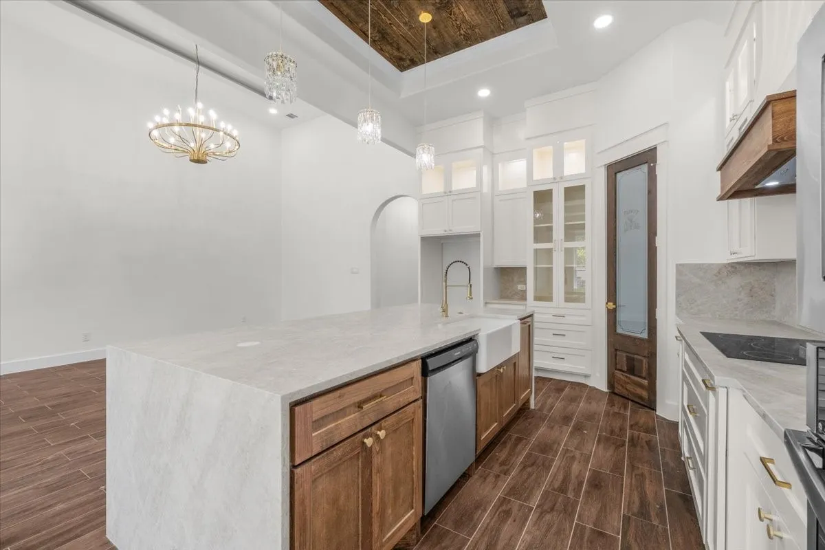 Kitchen featuring a large island with a stone countertop, wood-finish flooring, white cabinetry with display uppers, a farmhouse sink, and a dark wood door with frosted glass