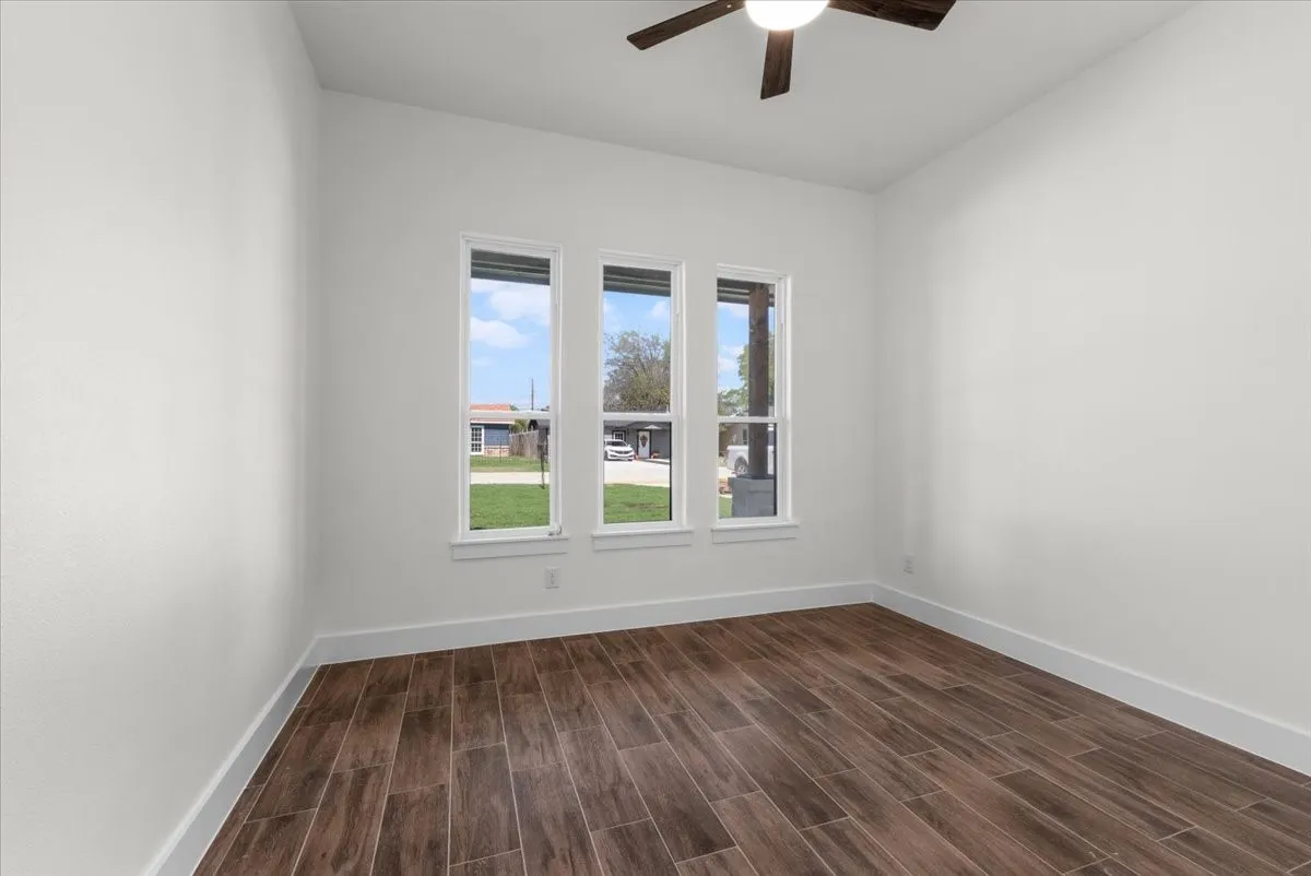 Wood-finish plank flooring with crisp white baseboards, three tall windows, and a ceiling fan