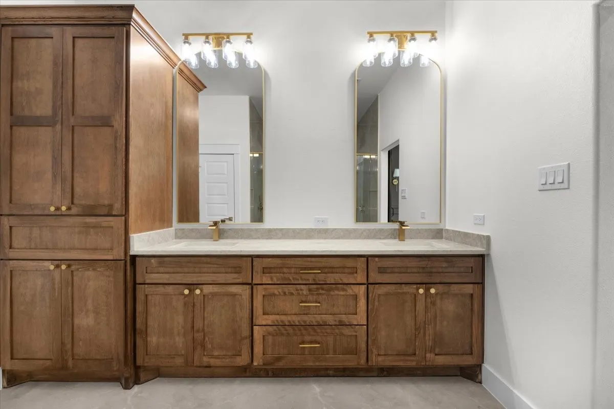Dual vanity with wood-finish cabinetry, light-toned countertop, and gold-finish​​‌​​​​‌​​‌‌​‌‌​​​‌‌​‌​‌​‌​​​‌​​ fixtures