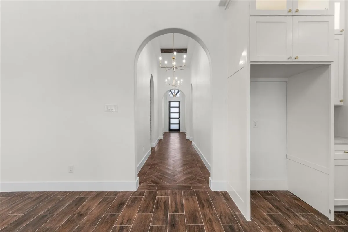 Hallway featuring wood-look tile flooring in a herringbone pattern, arched doorways, white walls, and contemporary light fixtures