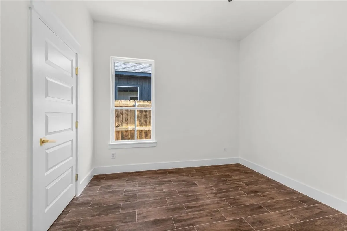 Wood-finish tile flooring, white interior door with gold-tone hardware, and a single window with white trim