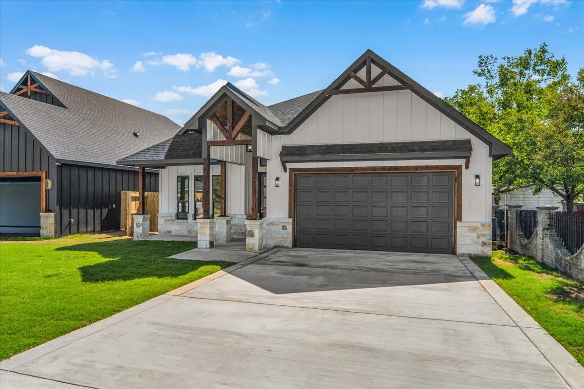 Modern farmhouse exterior featuring white vertical siding, exposed wood beams, stone accents, a dark gray garage door, and a concrete driveway
