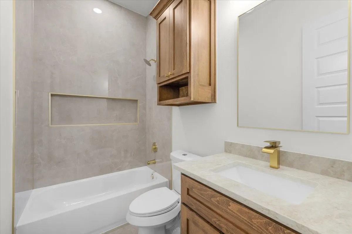 Tiled tub surround with recessed niche, integrated shower, and gold-finish fixtures