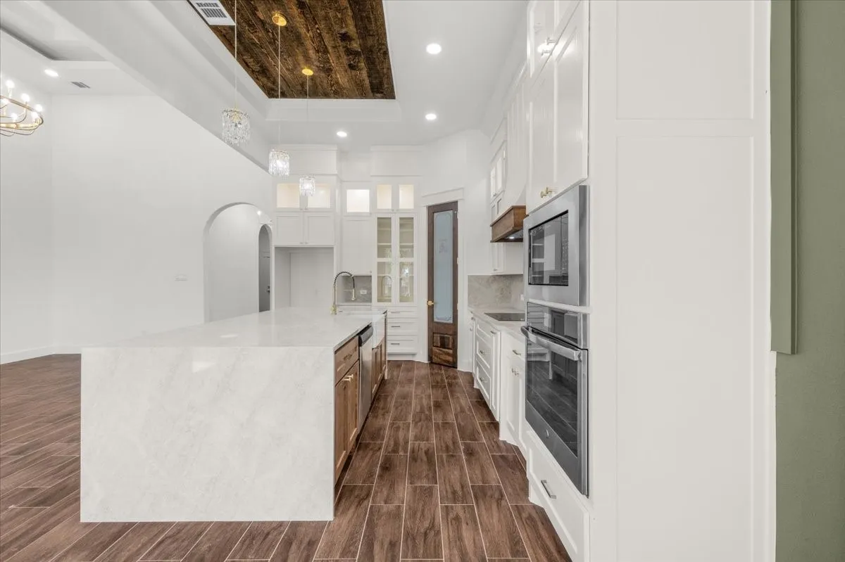 Expansive kitchen island with a waterfall countertop, integrated stainless steel dishwasher, and built-in double ovens