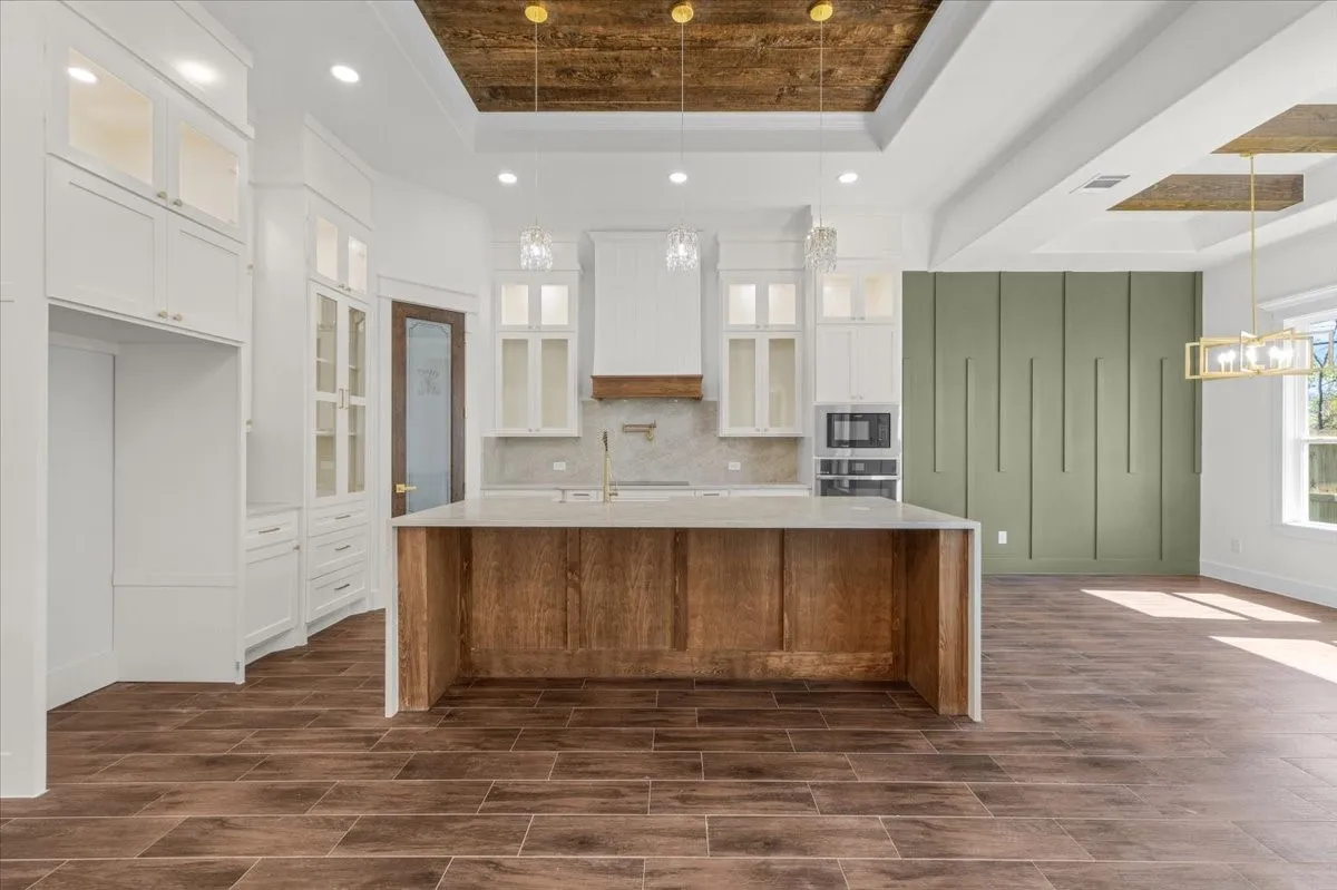 Wood-finish flooring throughout, featuring a kitchen island with stone countertop, white cabinetry with glass-front accents, and a distinctive wood plank ceiling detail