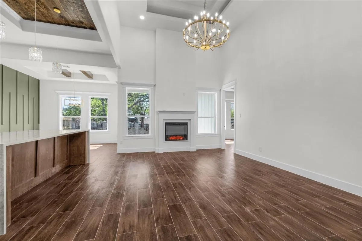High ceilings featuring a decorative chandelier, wood-finish flooring, a built-in electric fireplace, and a kitchen island with built-in cabinetry