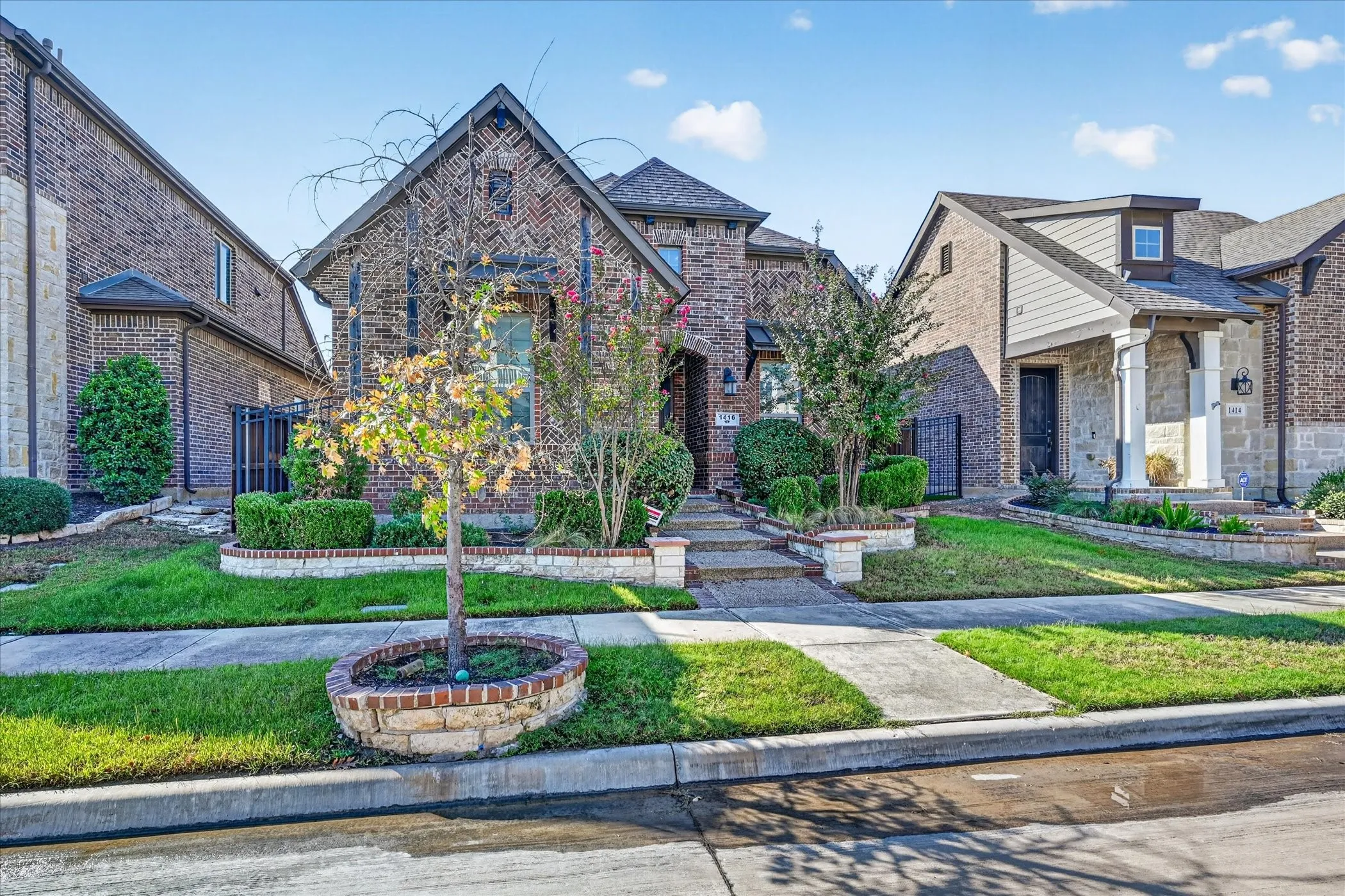 Brick facade with stone accents, gabled roofline, front porch with columns, landscaped yard, and concrete walkways