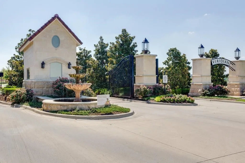 Stone-clad entry columns with decorative lanterns, a tiered fountain, and a stucco guardhouse with a tiled roof