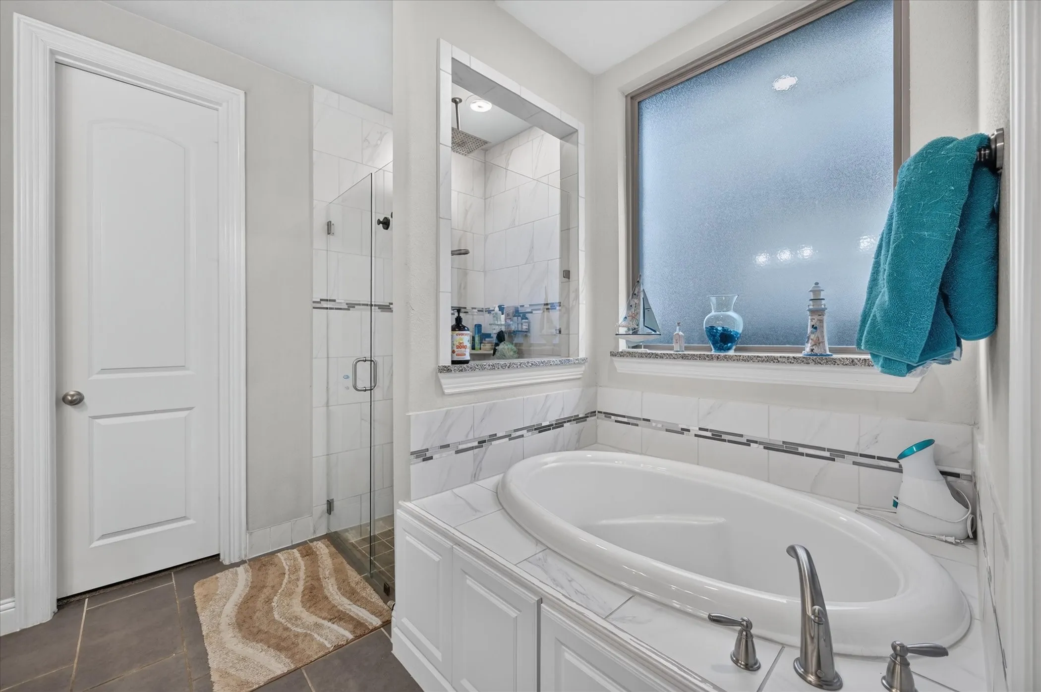 Soaking tub with brushed nickel fixtures, an enclosed glass shower, a tiled shower interior, and dark tile flooring