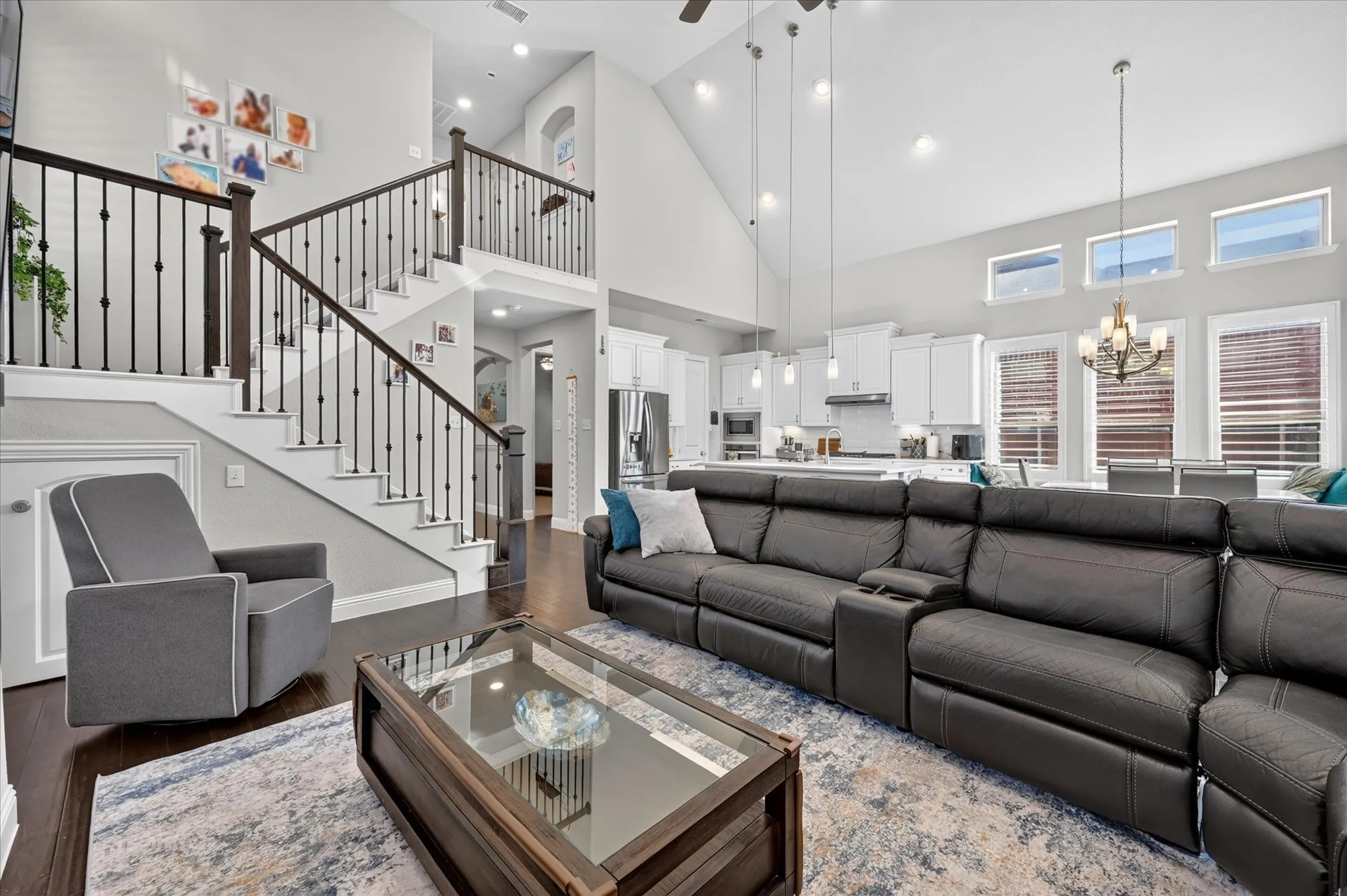 Open concept floor plan featuring vaulted ceilings, wood-finish flooring, a two-story staircase with iron balusters, and a kitchen with white cabinetry