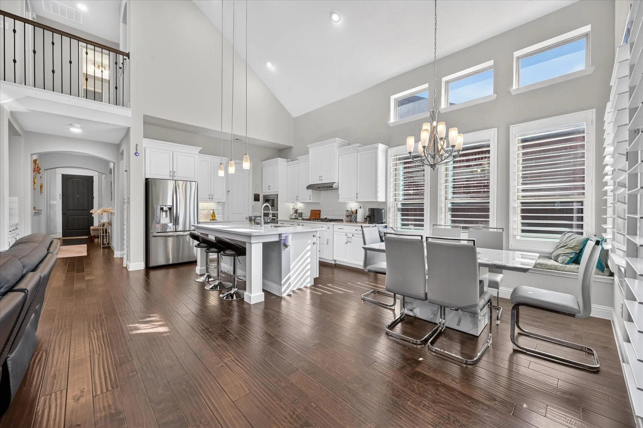 Vaulted ceiling, wood-finish flooring, white cabinetry, stainless steel appliances, and a kitchen island with pendant lighting