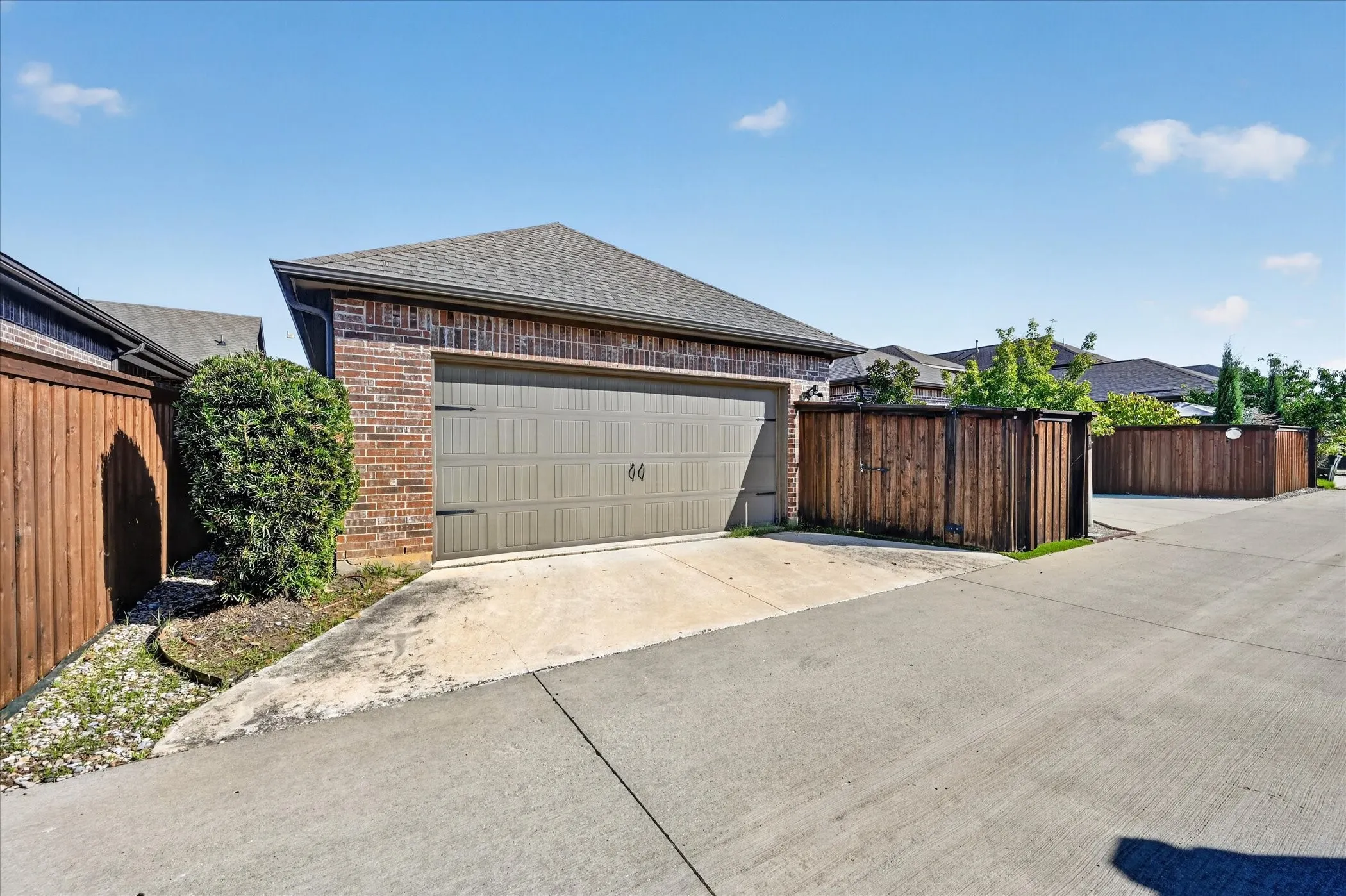 Brick exterior with an attached garage, wood privacy fencing, and a concrete driveway