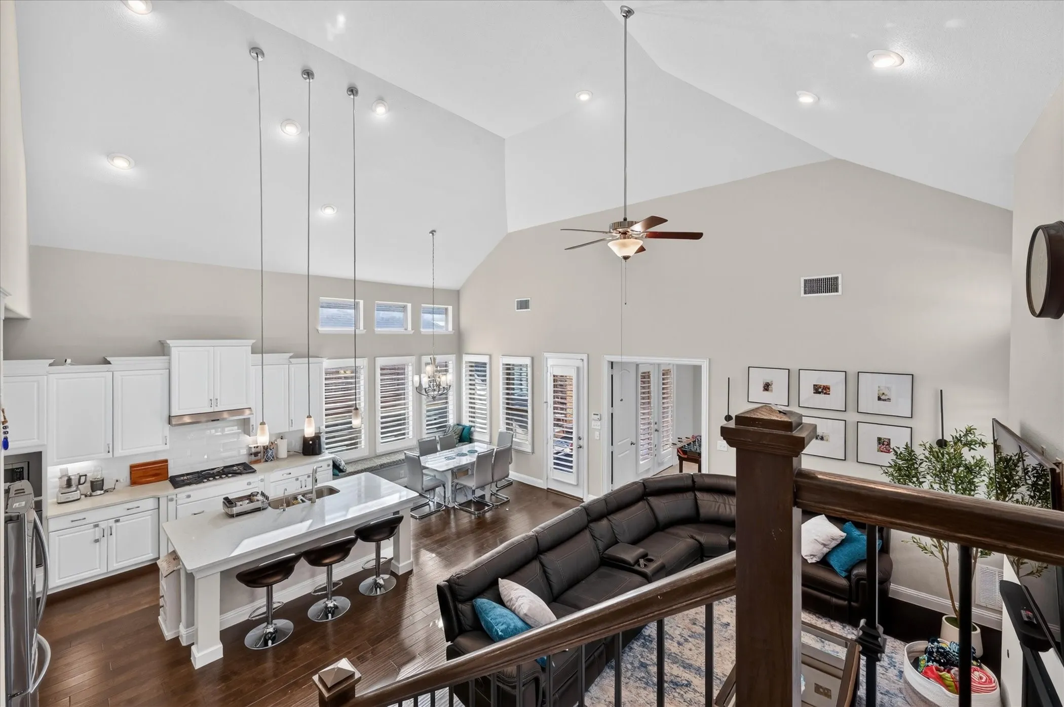 Vaulted ceilings, wood-finish flooring, white cabinetry, island with countertop seating, and recessed lighting