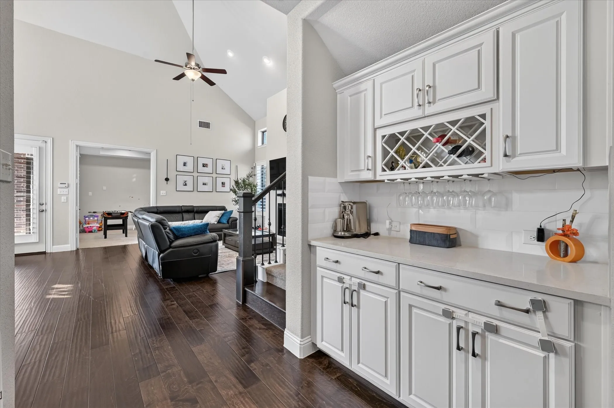 White cabinetry with integrated wine rack, light countertops, subway tile backsplash, and dark wood-finish flooring