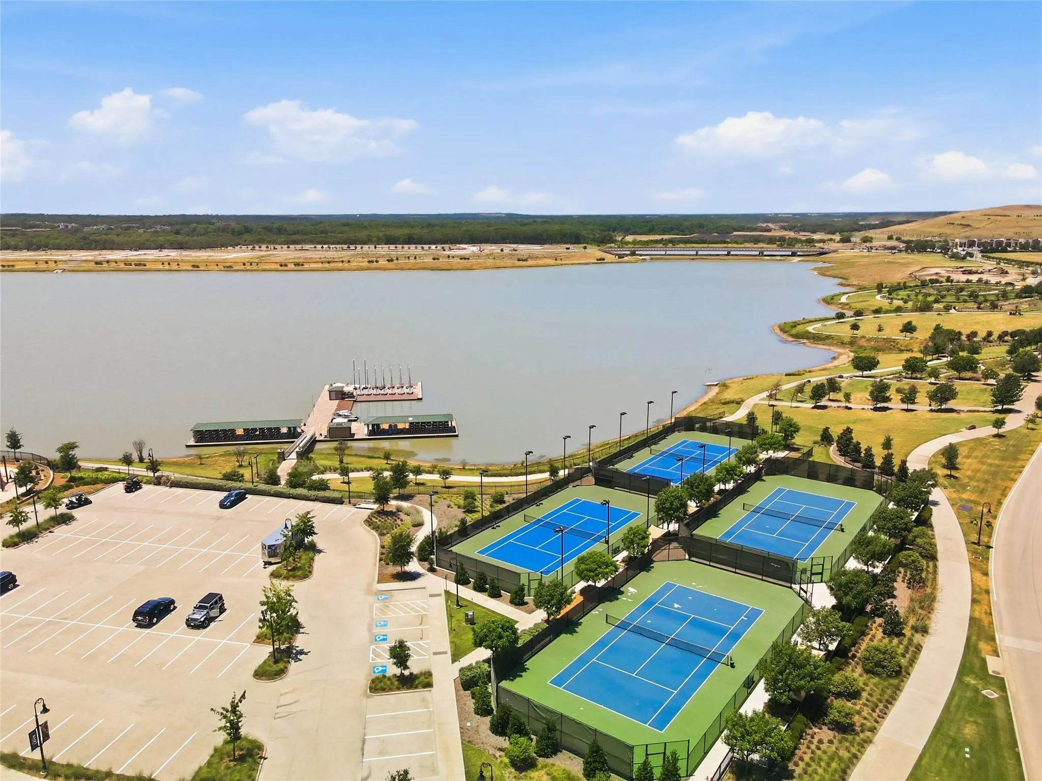 Expansive lakefront with a large dock, multiple tennis courts, and paved pathways
