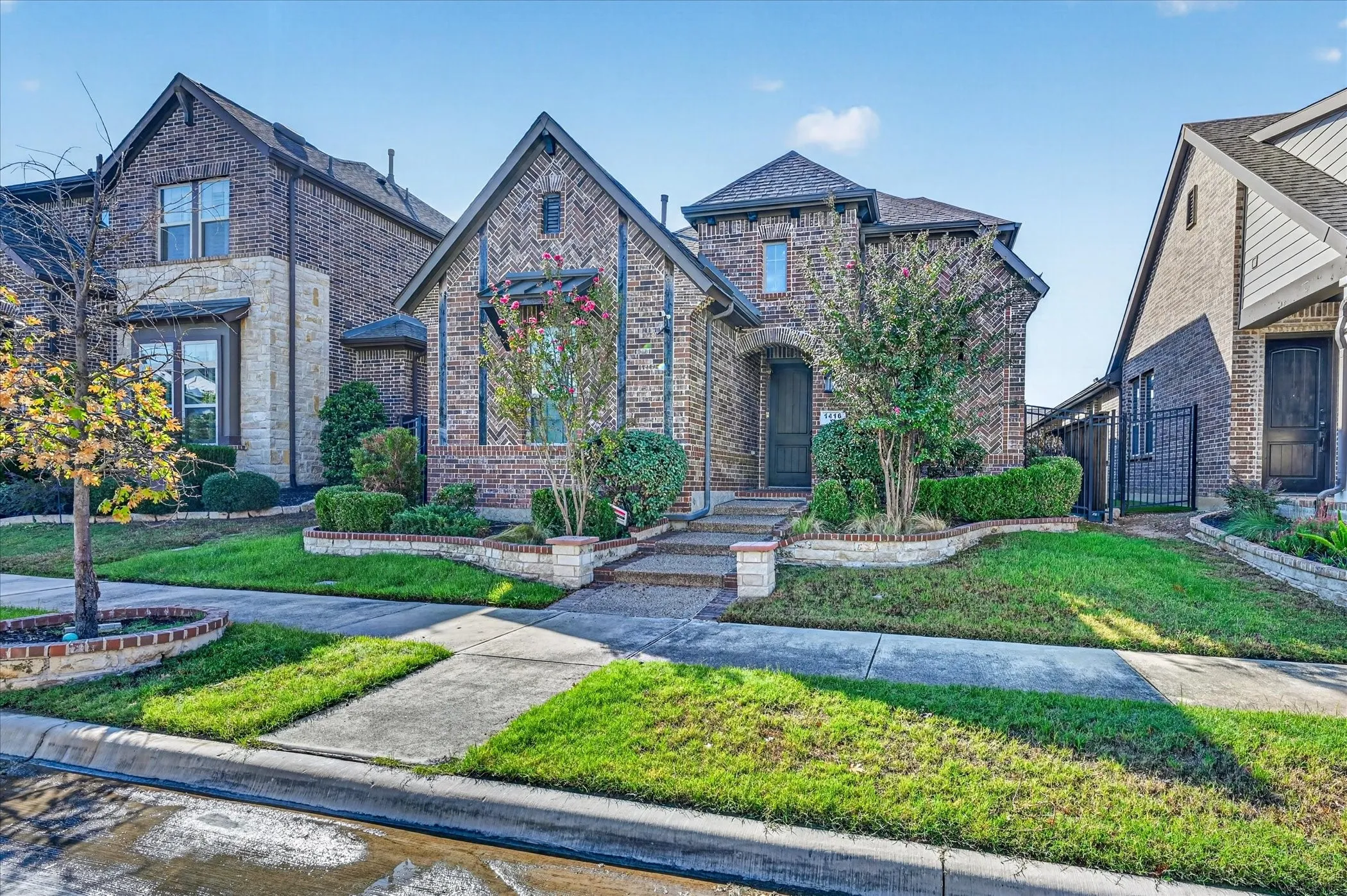 Brick exterior with stone accents, arched entry, mature landscaping, and an integrated garage