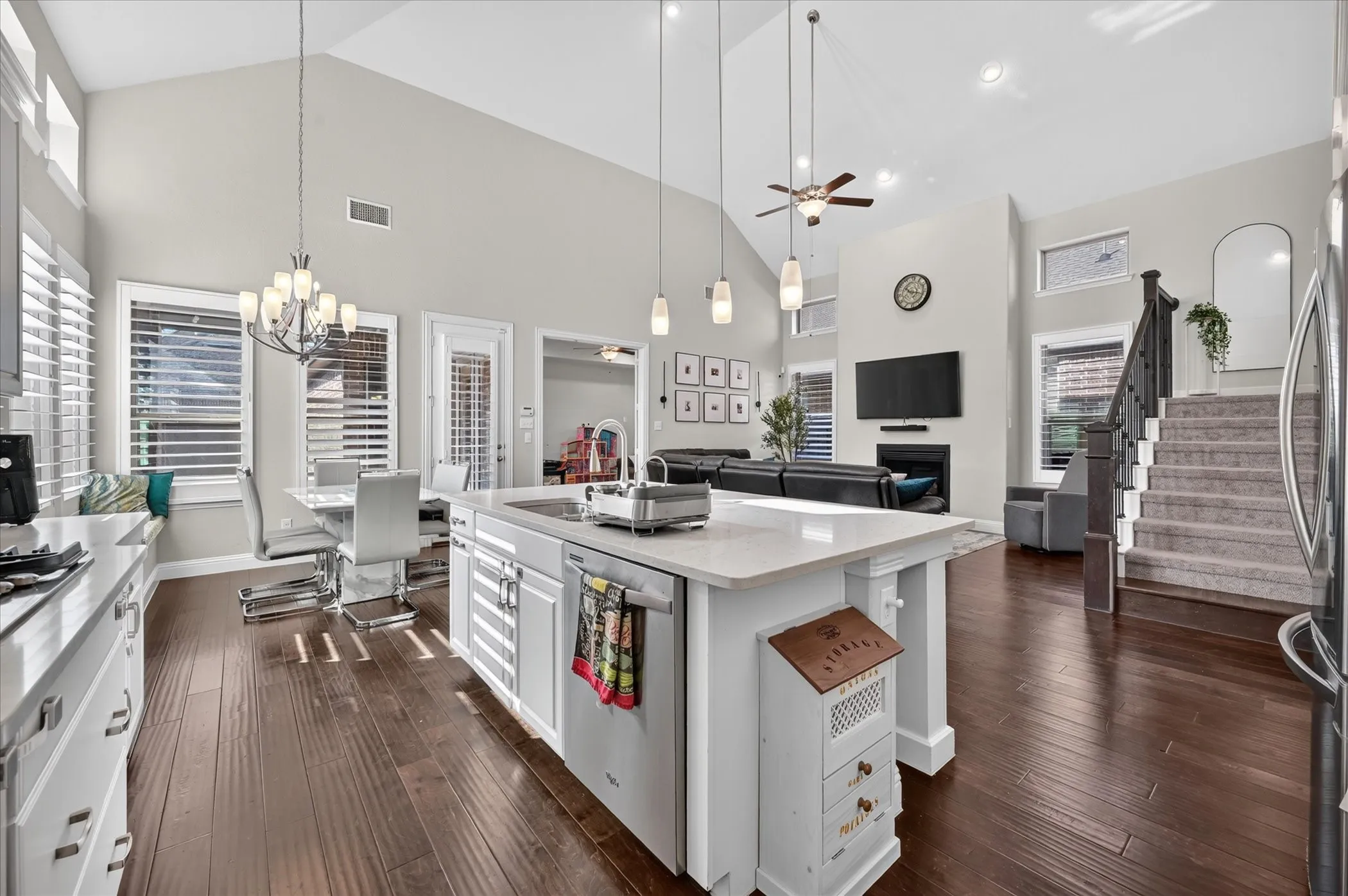 Open-concept living area featuring vaulted ceilings, wood-finish flooring, a kitchen island with stone countertops, a fireplace, and a staircase with carpeted treads