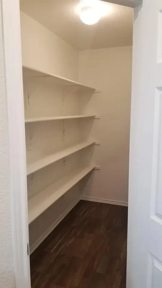 Walk-in pantry featuring multiple white shelves and wood-finish flooring