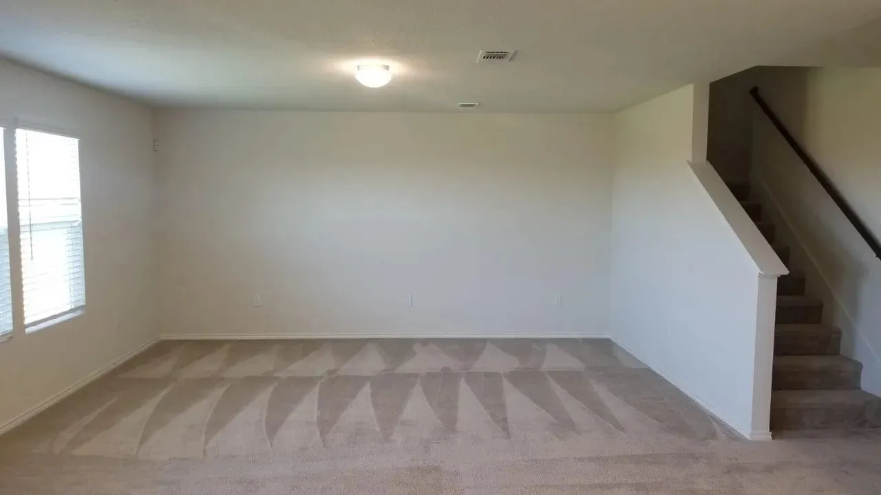 Carpeted living area featuring white walls, dual windows with blinds, a flush mount ceiling light, and a staircase with a dark handrail