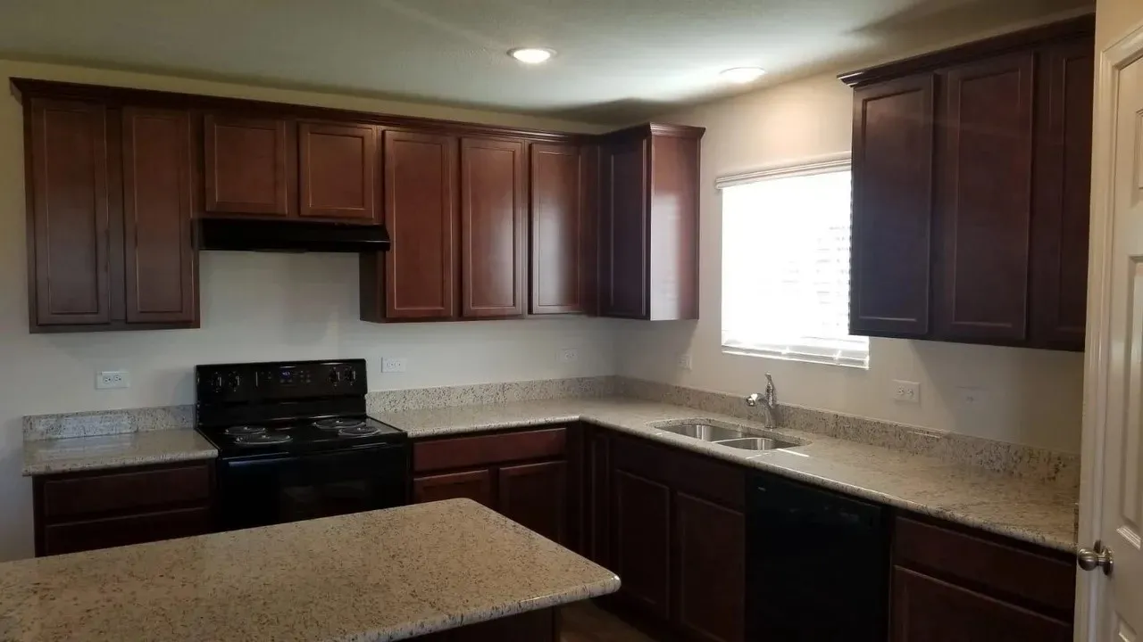 Kitchen featuring dark wood-finish cabinetry, light-toned countertops, stainless steel sink with pull-down faucet, and built-in black appliances