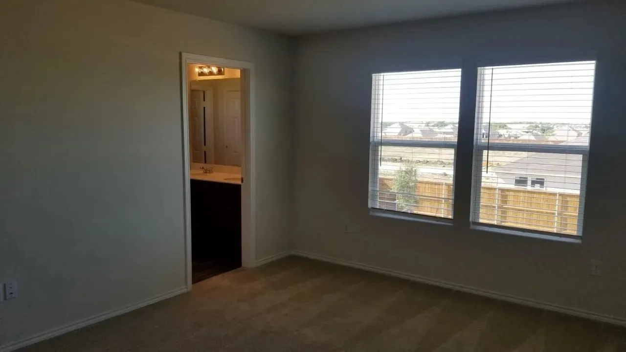 Master Bedroom Neutral wall paint, carpet flooring, two windows with blinds, and a doorway to a bathroom featuring a vanity with a countertop and a light fixture