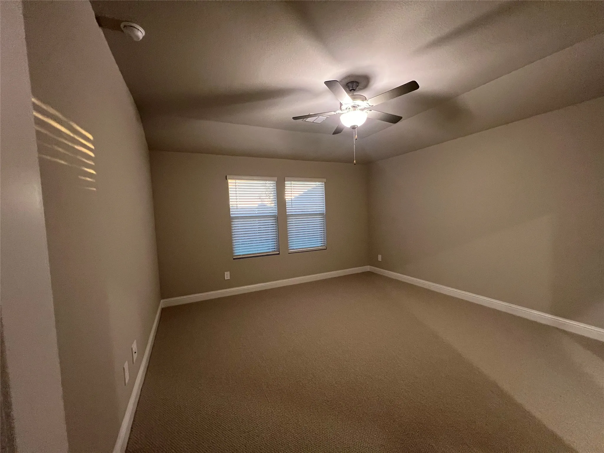 Carpeted room featuring a ceiling fan with integrated lighting, two windows with horizontal blinds, and neutral-toned walls