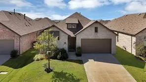 Stone and brick facade home featuring an attached garage, a concrete driveway, and a front yard with mature landscaping