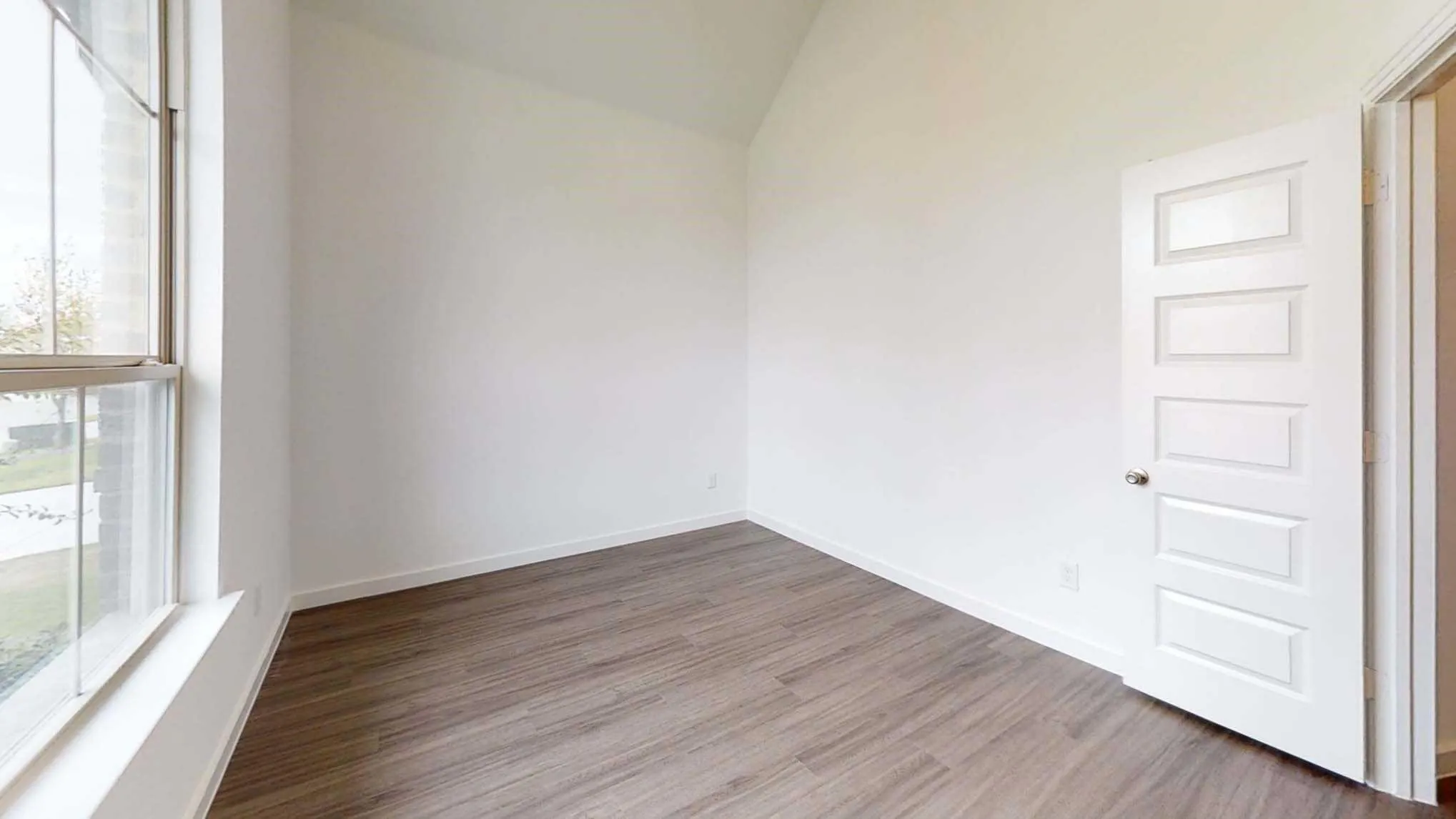 Vaulted ceiling, large window, wood-finish flooring, white paneled door, and neutral wall tones