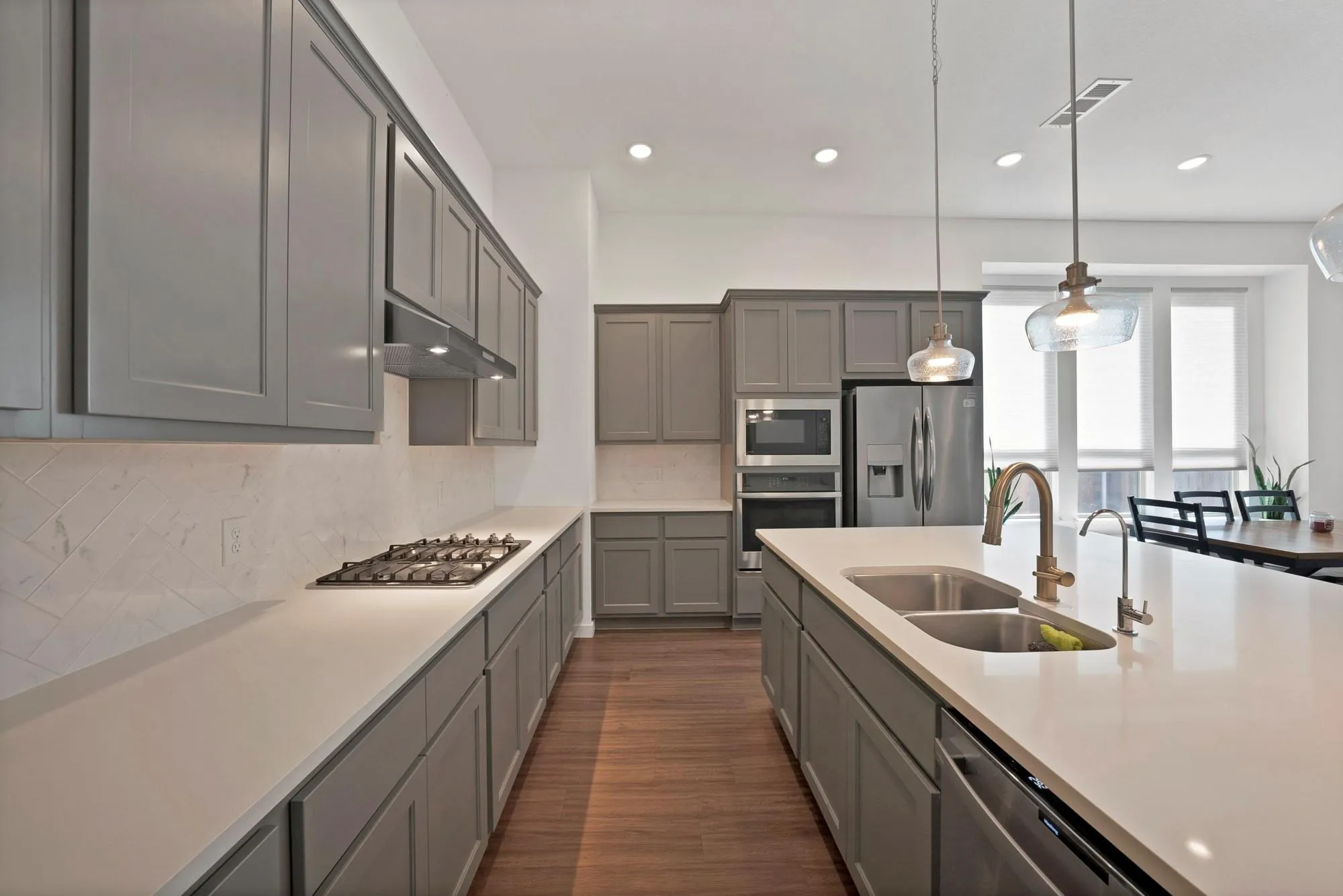 Contemporary kitchen featuring gray shaker cabinetry, stainless steel appliances, a gas cooktop, and a spacious island with a double basin sink