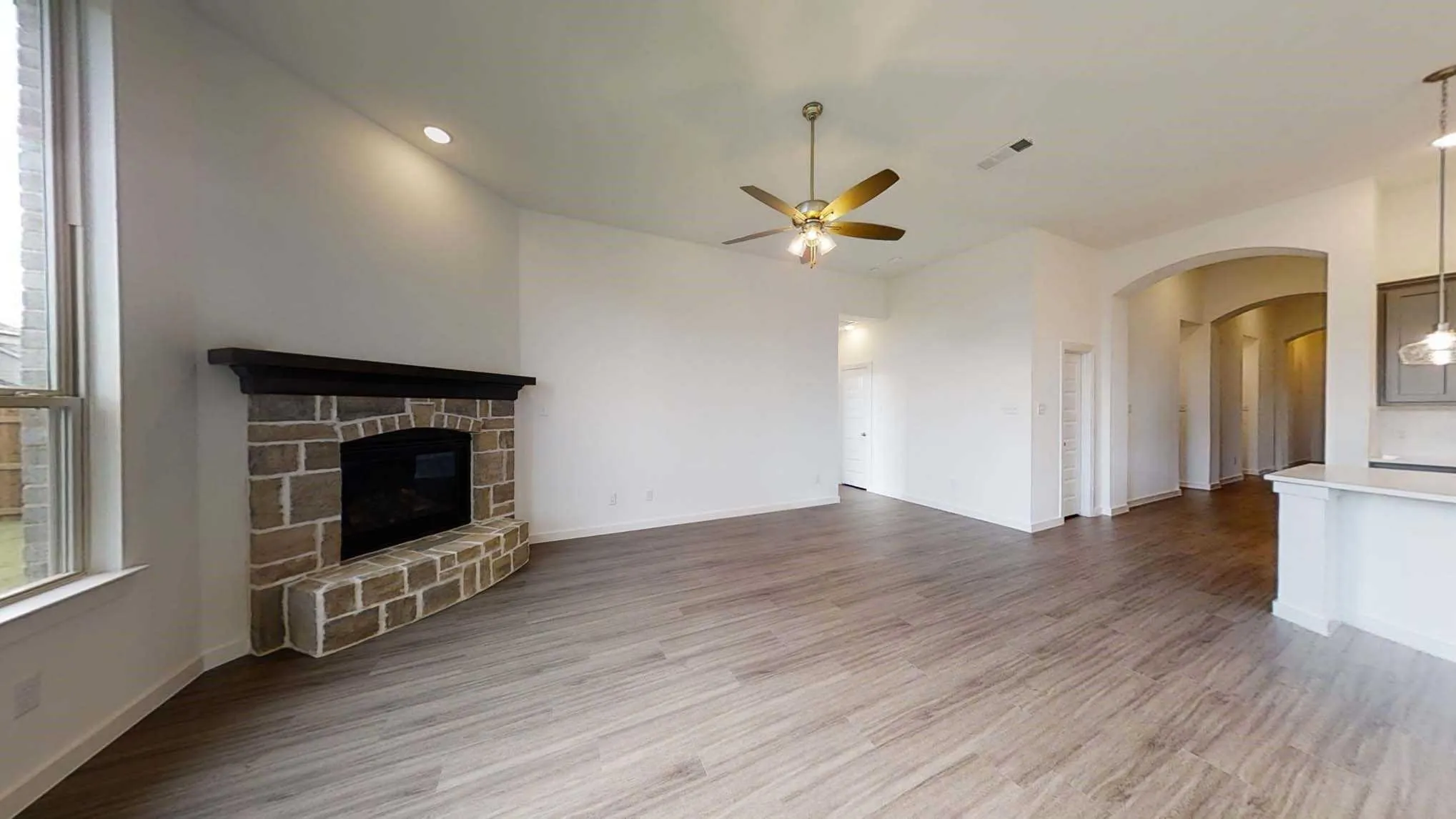 Stone-clad fireplace with dark wood mantel, wood-finish flooring, recessed lighting, ceiling fan, and arched entryway