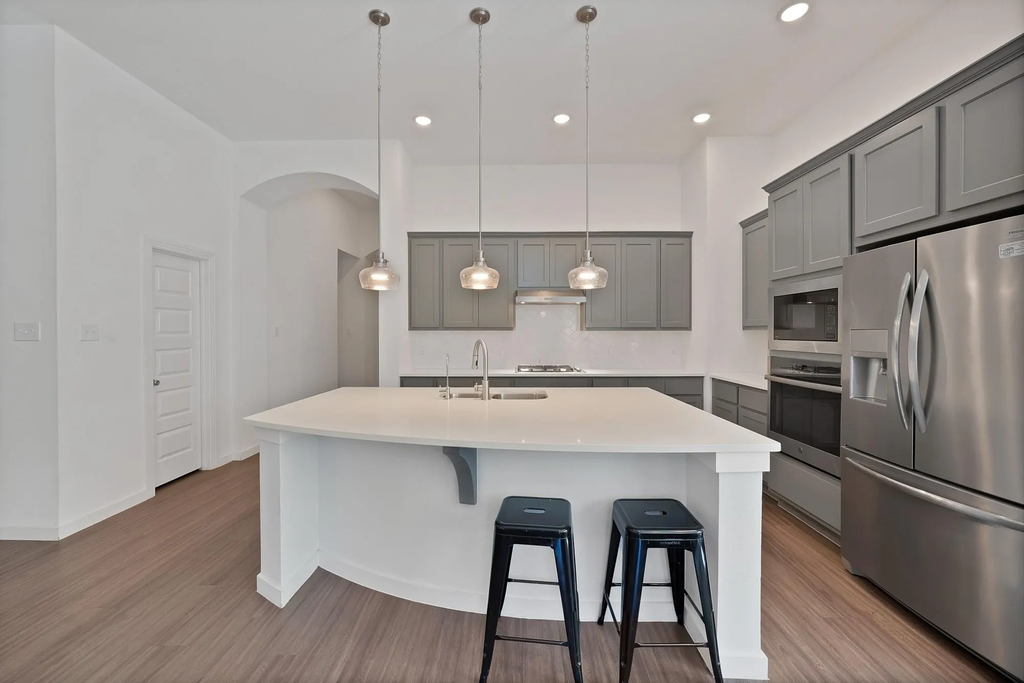 Kitchen featuring an expansive island with a white countertop, gray cabinetry, stainless steel appliances, and wood-finish flooring