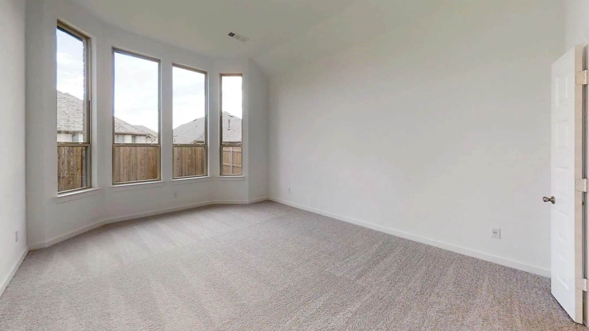Expansive room featuring a bay window with multiple vertical panes, light-colored carpeting, a neutral wall finish, and a paneled door