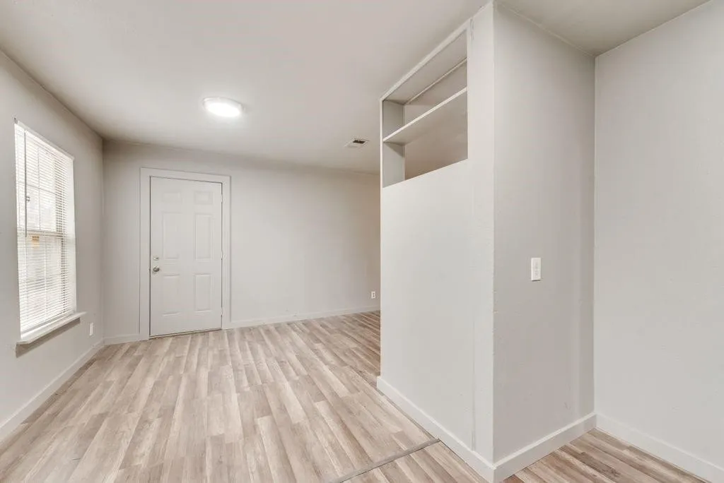 Wood-finish flooring, built-in shelving, white paneled door, and a flush-mount ceiling light