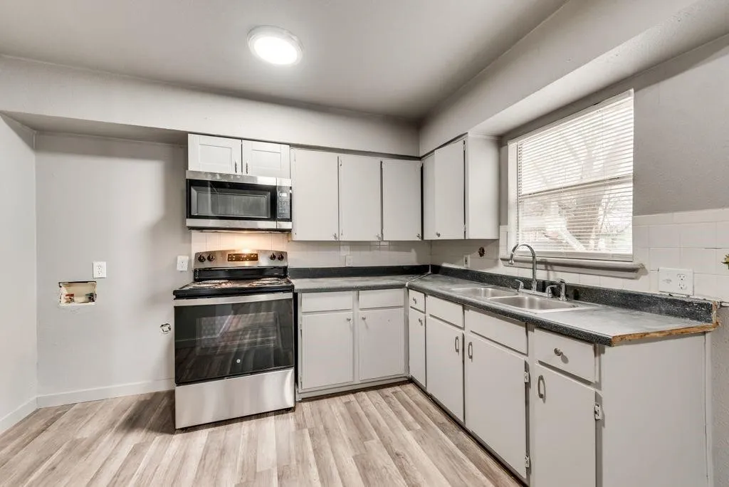 Kitchen featuring wood-finish flooring, white cabinetry, stainless steel appliances, a dual basin sink, and a window